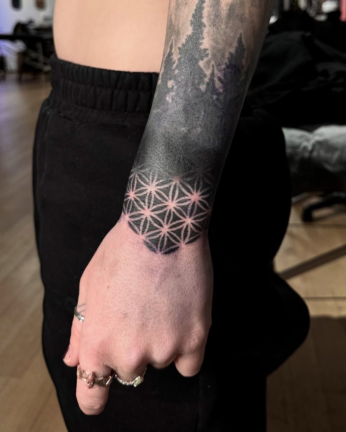 Geometric flower-of-life tattoo on a wrist transitioning into a blackout forearm sleeve.