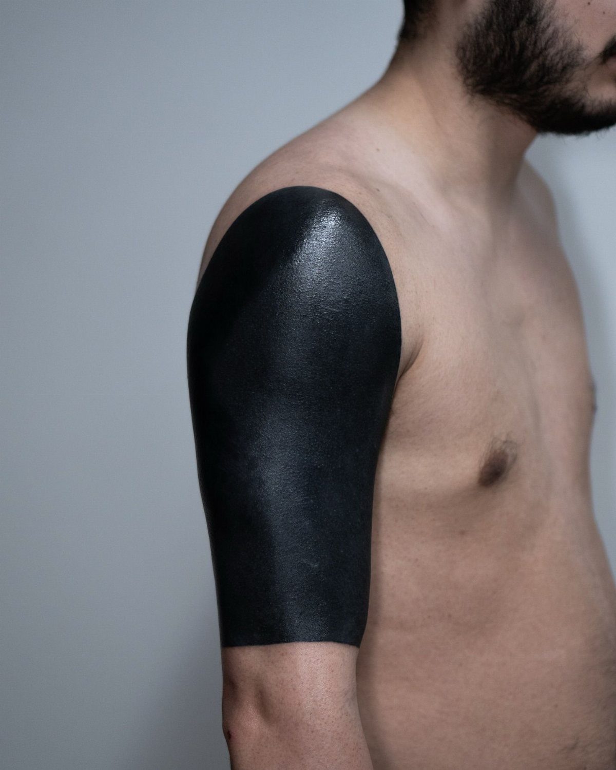 Man's upper arm and shoulder covered in a solid black ink blackout tattoo.
