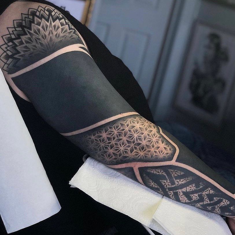 Man's arm with a blackwork tattoo featuring complex geometric patterns and solid black sections.