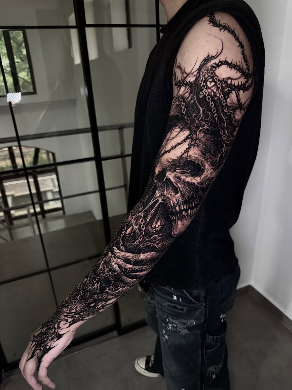 Detailed skull and gothic tattoo covering a man's entire arm from shoulder to hand.