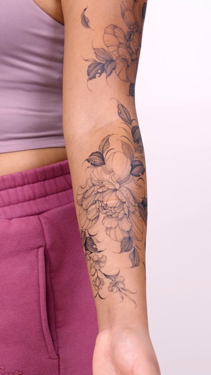 Detailed black and grey floral tattoo on a woman's forearm featuring peony blossoms.