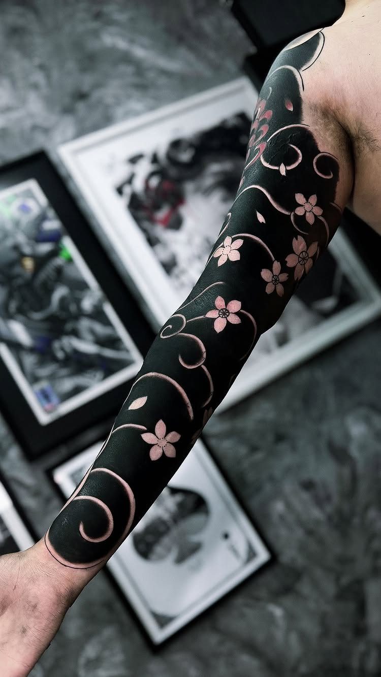 Blackout tattoo on a forearm with negative space flowers and swirling vines.
