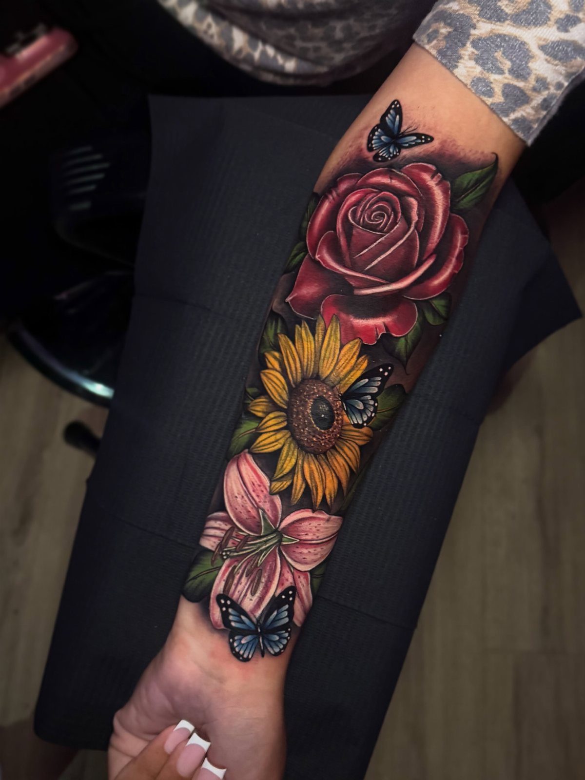 Floral tattoo sleeve with red rose, sunflower, and blue butterflies on a forearm