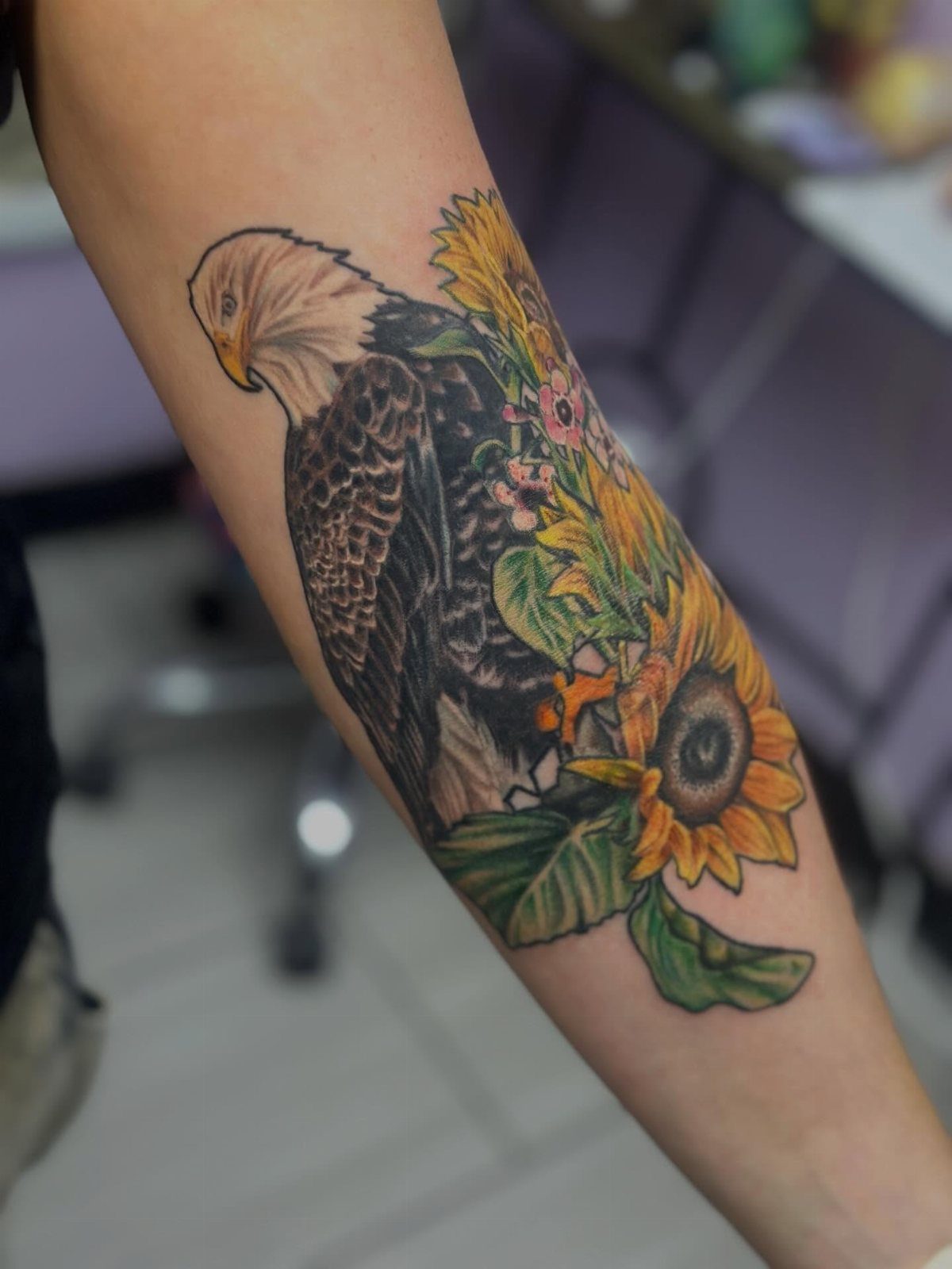 Bald eagle tattoo with yellow sunflowers on a person's forearm