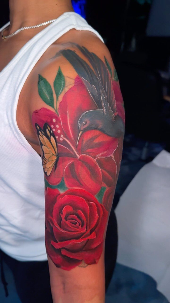 Colorful floral tattoo with a bird and butterfly on a woman's upper arm