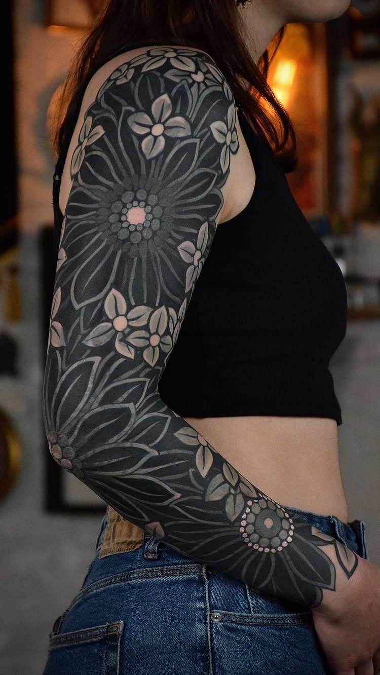 Woman's arm with a full-sleeve floral and mandala tattoo in dark grey ink