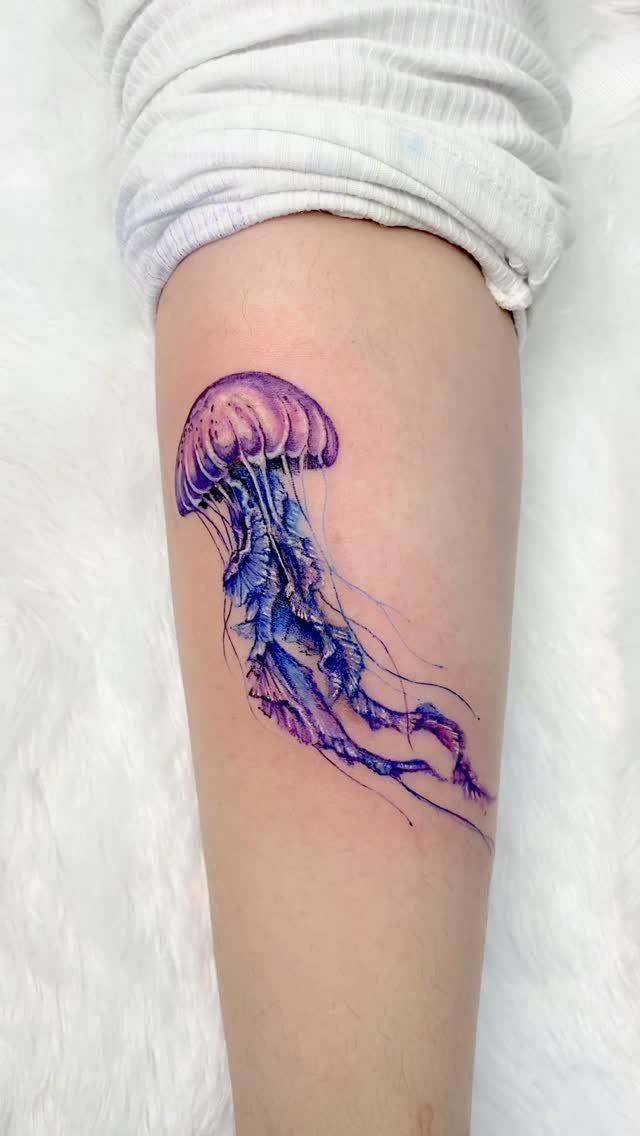 Purple and blue jellyfish tattoo on a person's leg against white fur.