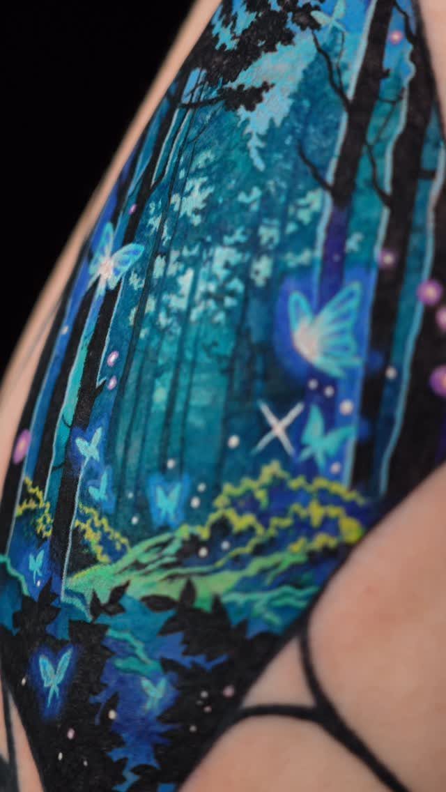 Mystical forest tattoo with glowing blue butterflies and teal trees on skin.