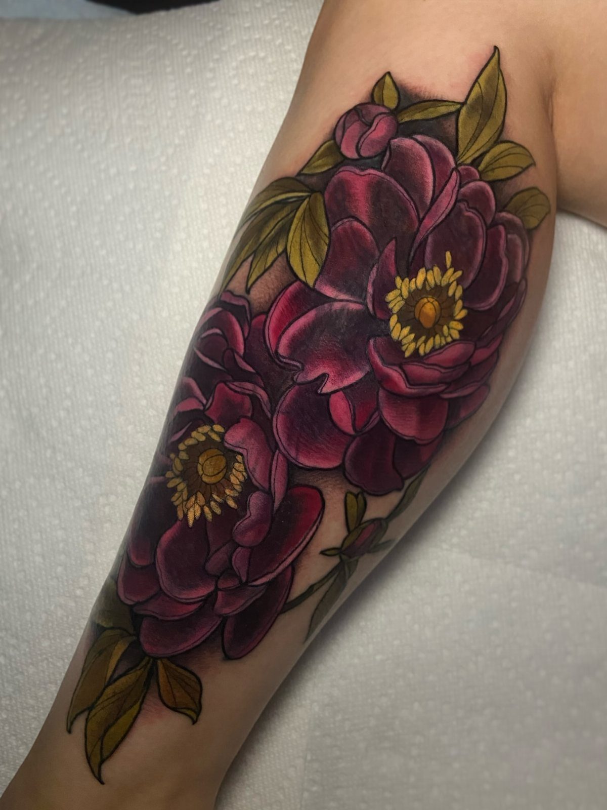 Neo-traditional tattoo of deep purple peonies with yellow centers on a person's arm.