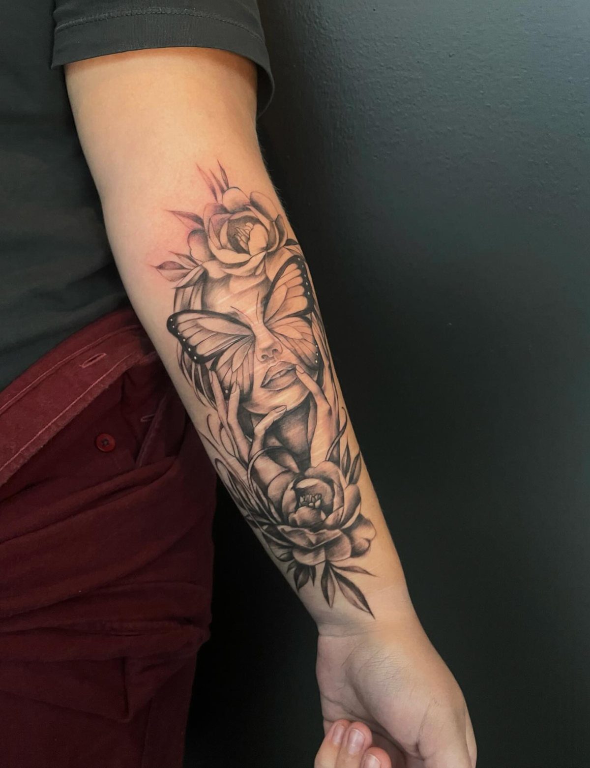 Forearm tattoo of a woman's face with a butterfly and roses.