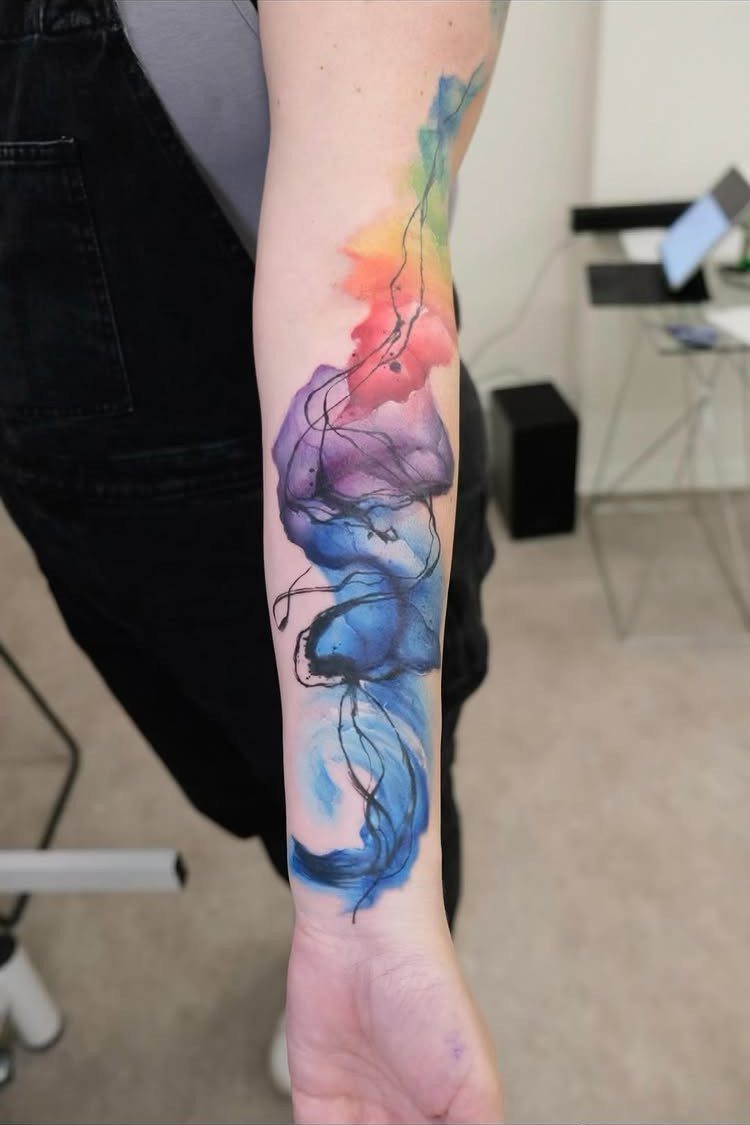Watercolor tattoo on a forearm with vibrant blue, purple, and yellow blended colors.