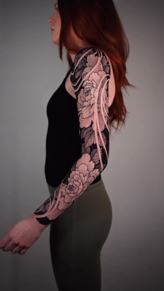Woman with red hair showing a detailed floral sleeve tattoo on her arm.