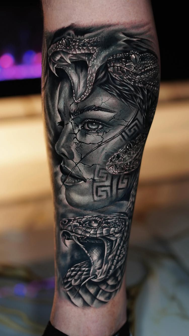 Detailed black and grey tattoo of a cracked stone face with snakes on an arm