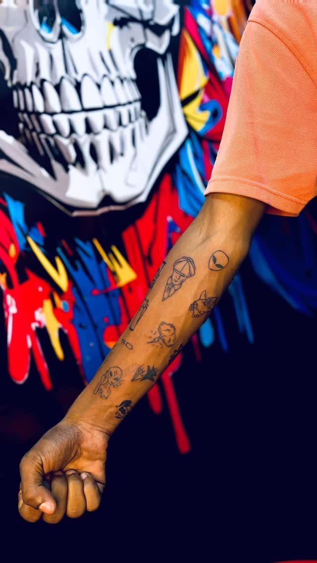 Forearm with small minimalist black ink tattoos against a colorful graffiti skull background