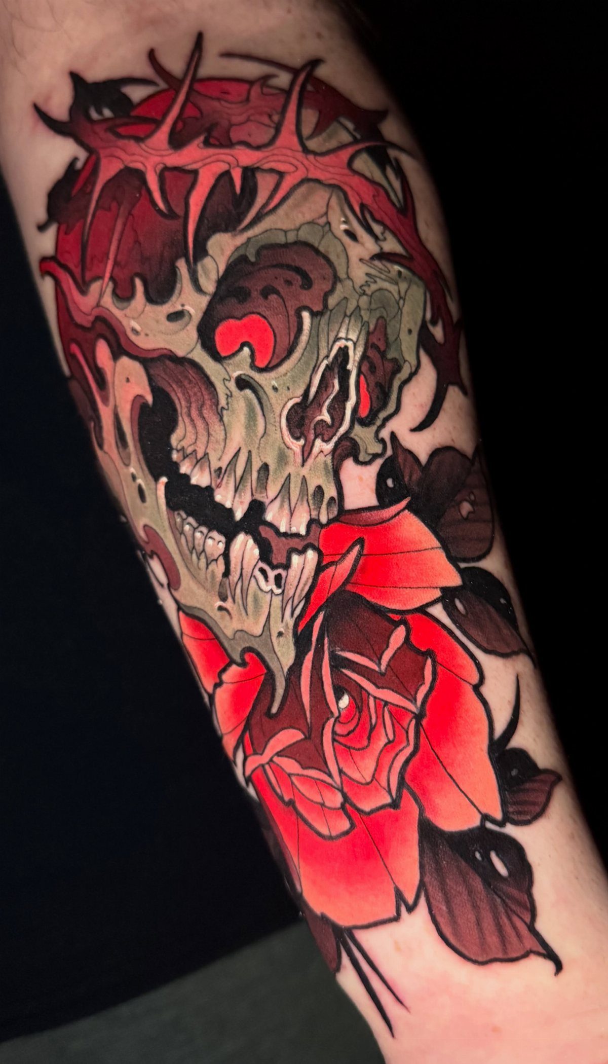 Skull and red rose tattoo with thorns on a person's forearm.