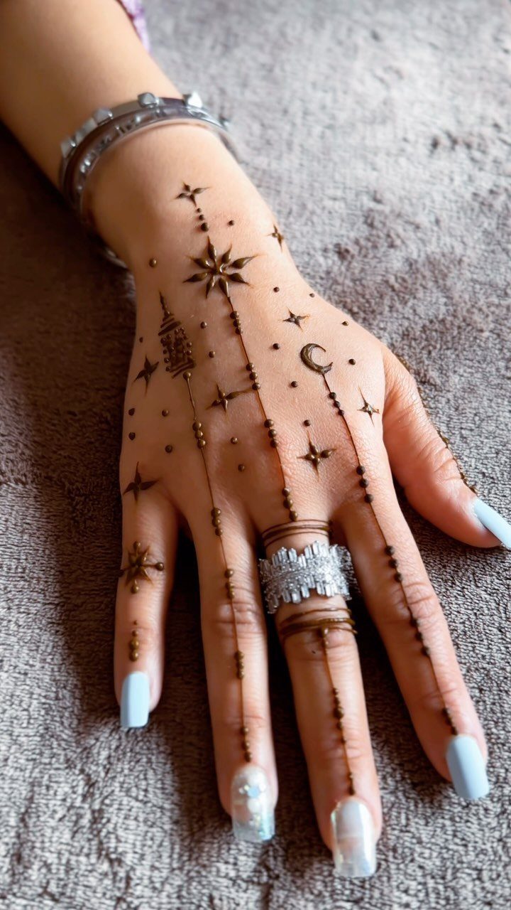 Hand with intricate brown henna star and moon tattoos and light blue nails.