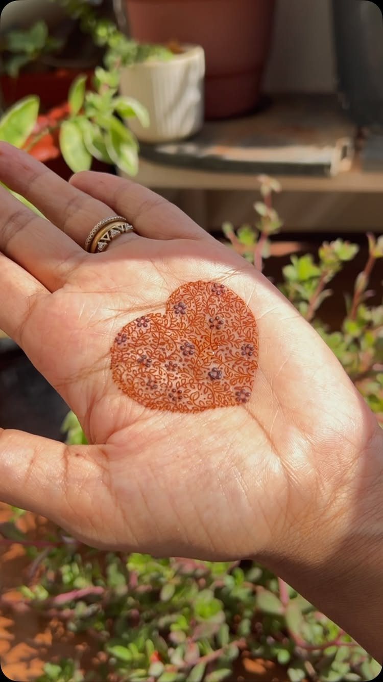 Heart-shaped henna tattoo with floral details on the palm of a hand.