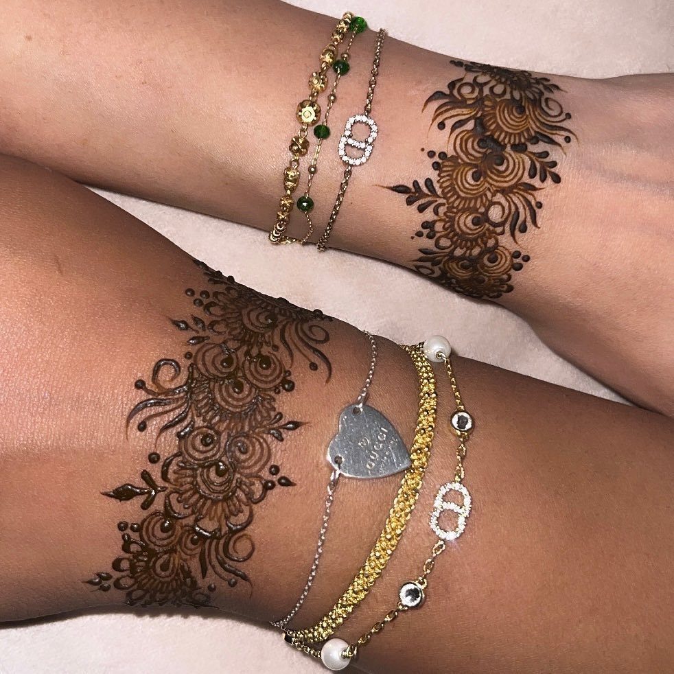 Intricate brown henna designs on two wrists adorned with gold and silver bracelets.