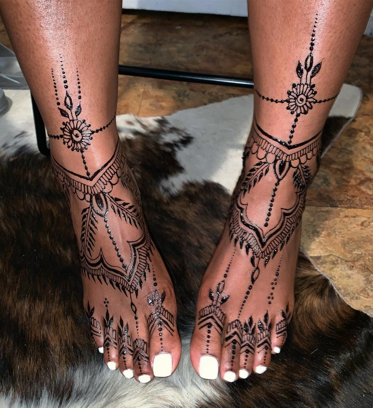 Intricate black henna tattoos on the tops of feet and ankles with white toenails.