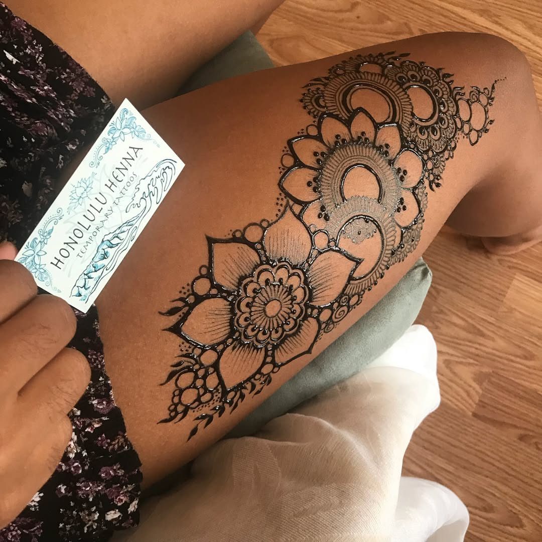 Intricate brown henna mandala and floral tattoo on a person's leg.