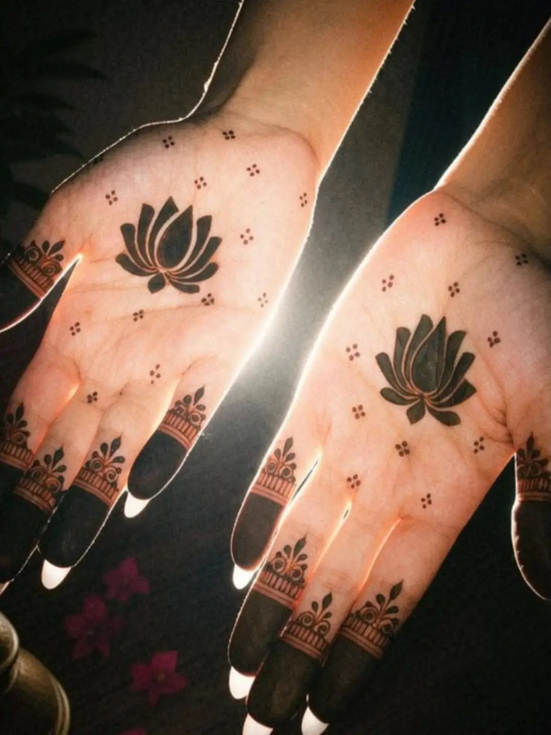 Lotus flower henna designs on two open palms with decorated fingers