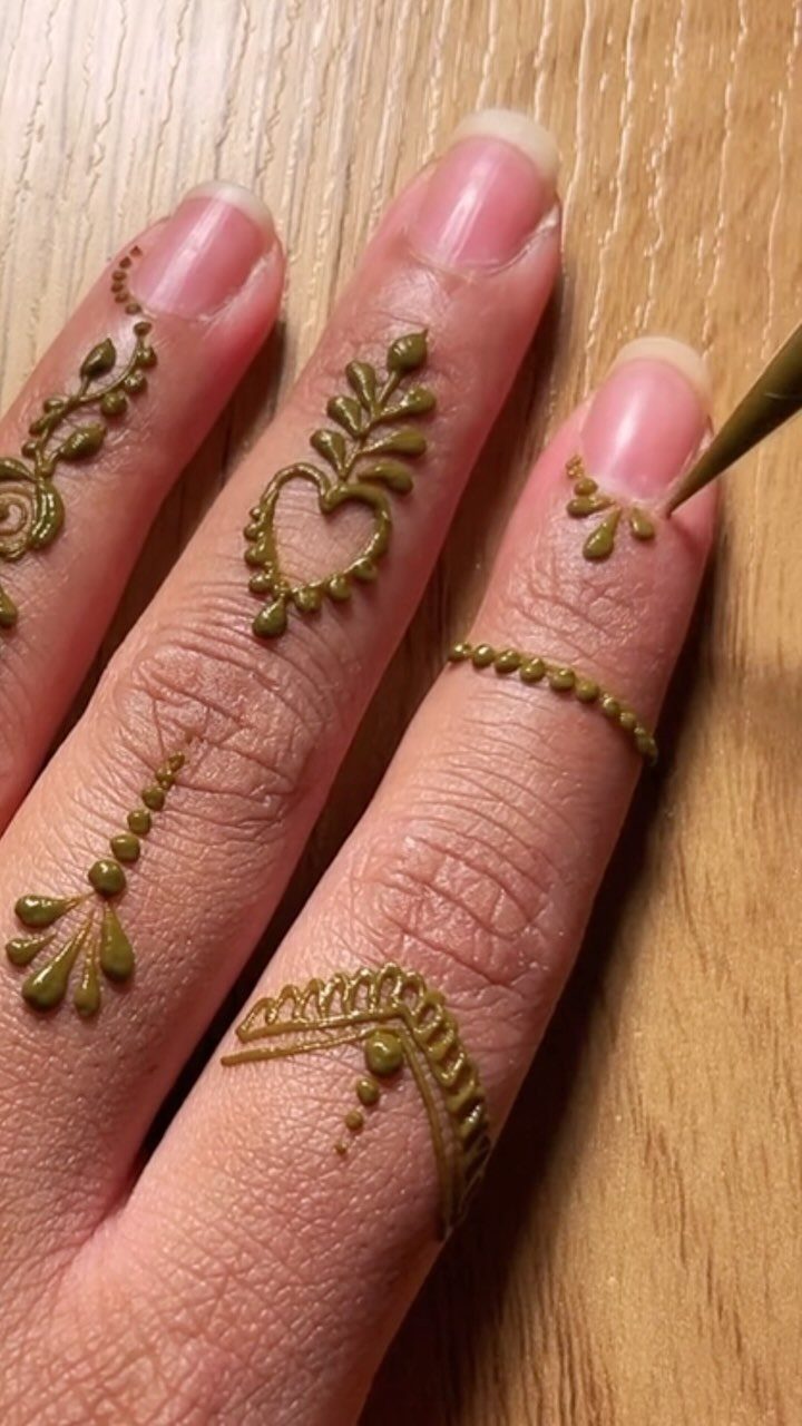 Green henna paste patterns and dots being applied to three fingers on wood.