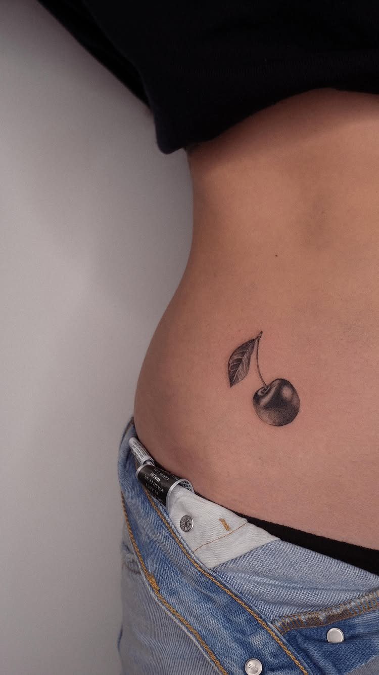 Small cherry tattoo with a leaf on a person's hip and waist.