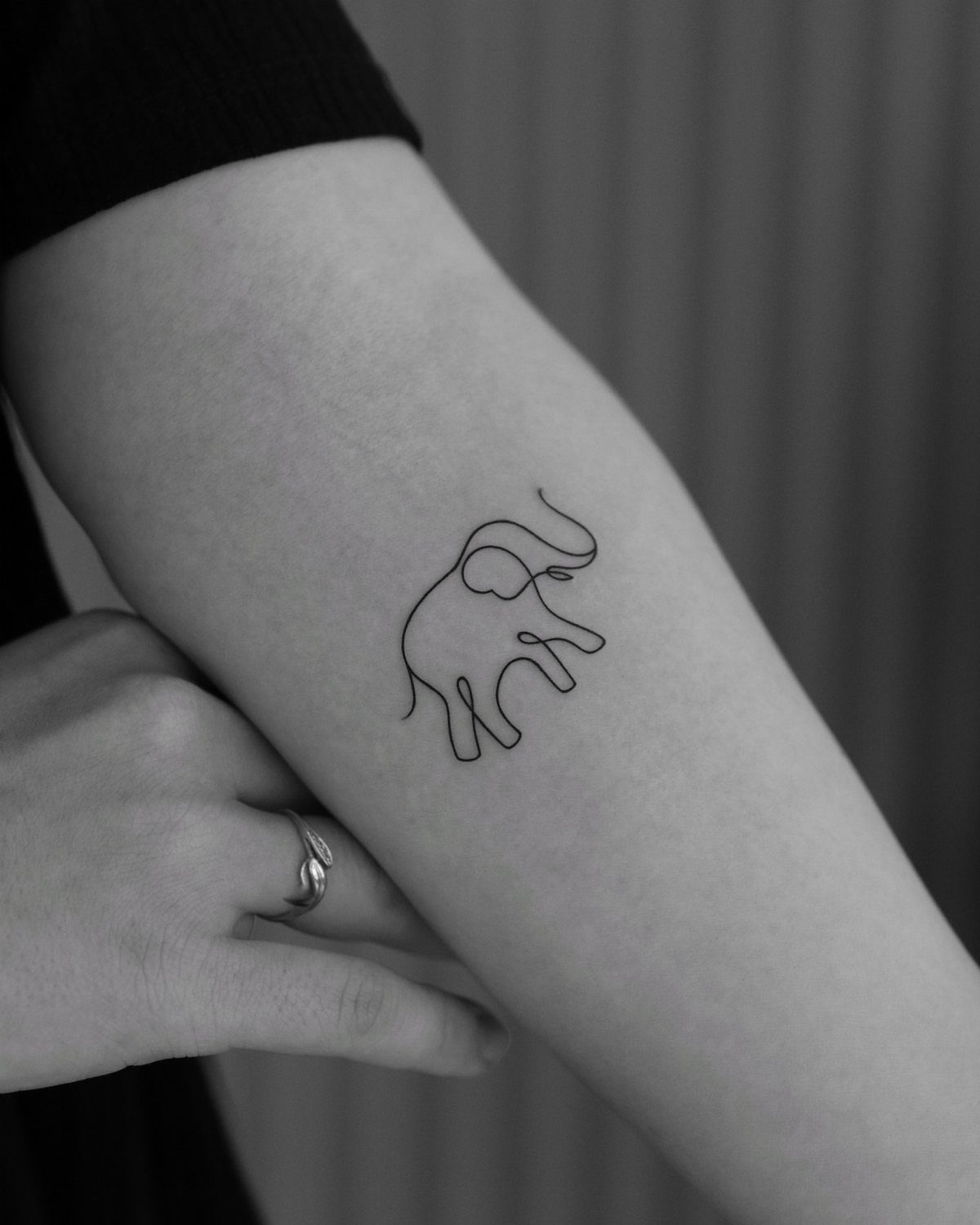 Minimalist elephant line-art tattoo on a person's forearm in black and white.