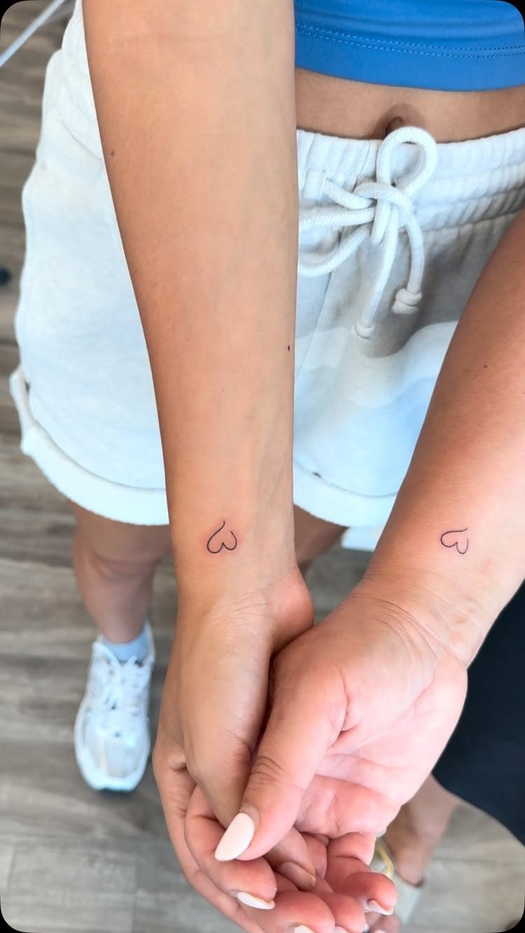 Small heart outline tattoos on the inner wrists of two people holding hands.