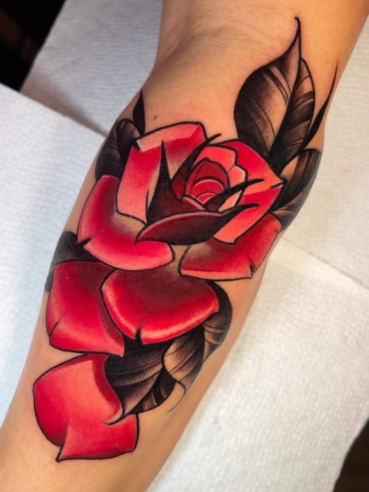 Red rose tattoo with black leaves on a person's forearm.