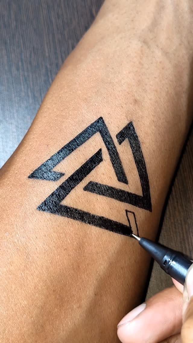 Black ink pen drawing a geometric triangular fake tattoo on a forearm.