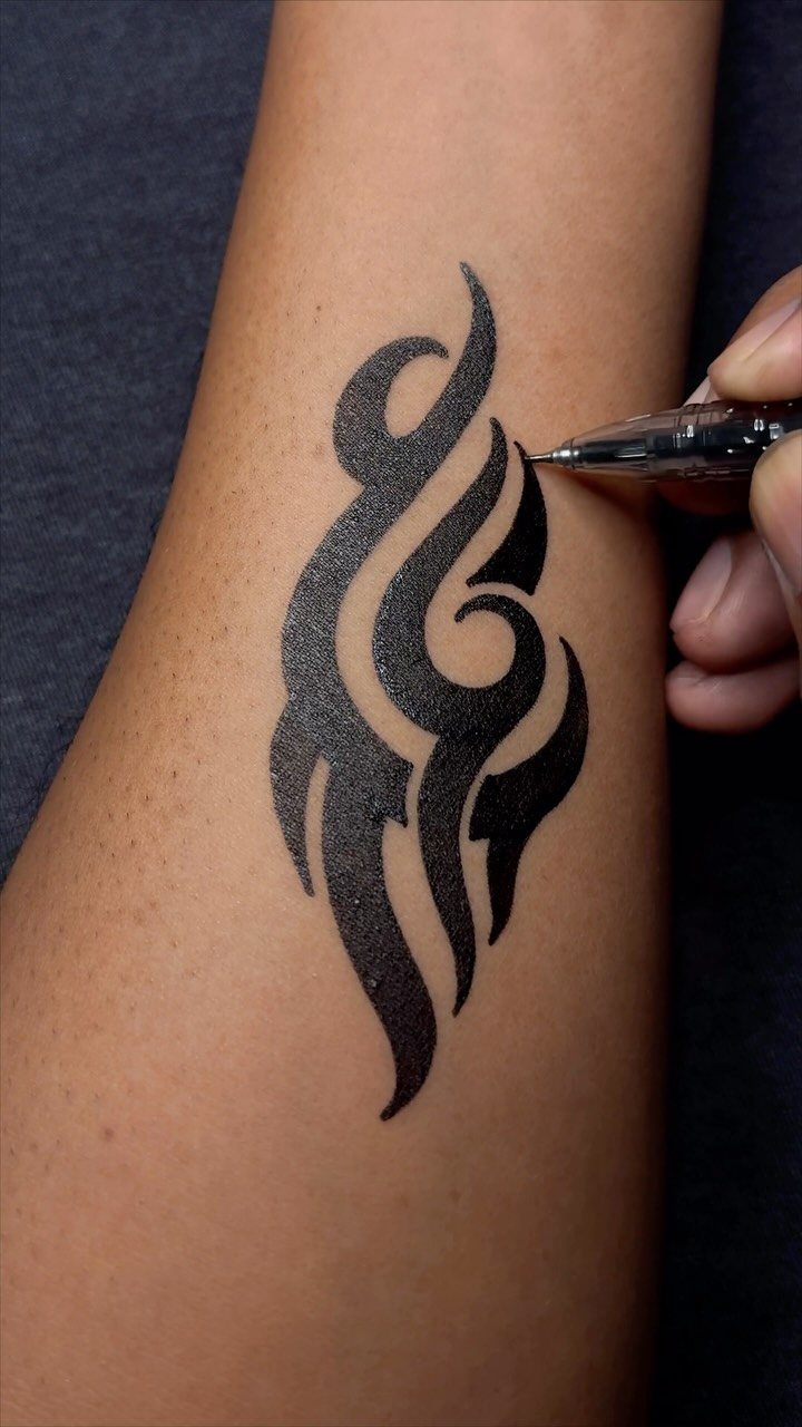 Black ink pen drawing a tribal tattoo design on a person's forearm