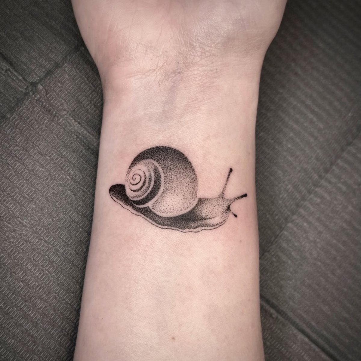 Snail tattoo on a wrist created with detailed black ink dotwork shading