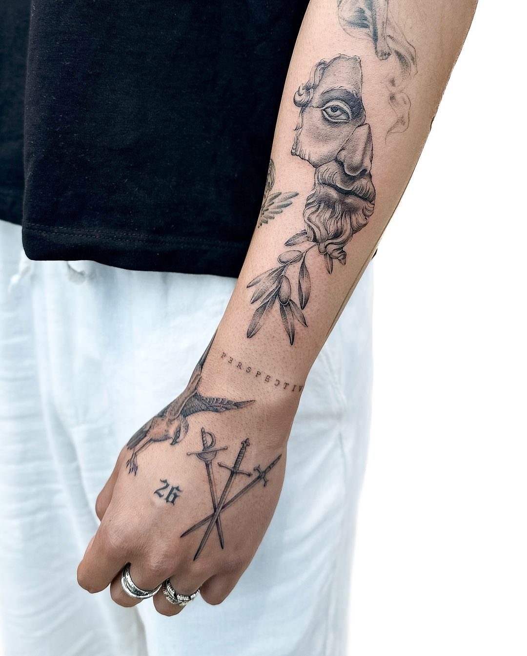 Forearm and hand with minimalist fine line tattoos of a statue and swords.