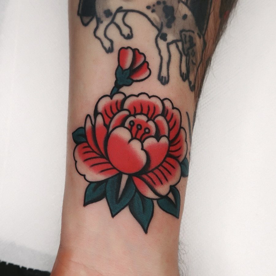 Red peony flower tattoo with green leaves on a person's forearm
