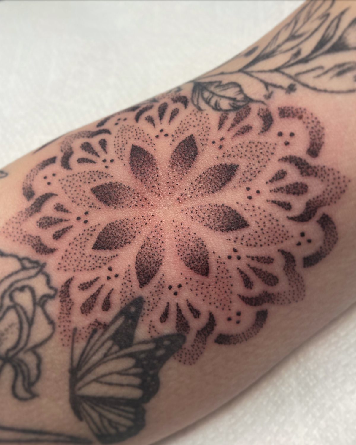 Mandala tattoo with dotwork shading filling a gap between other arm tattoos.