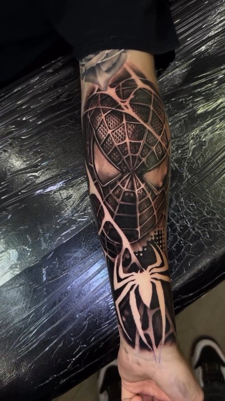 Spider-Man tattoo on a forearm featuring a mask and spider emblem in black ink