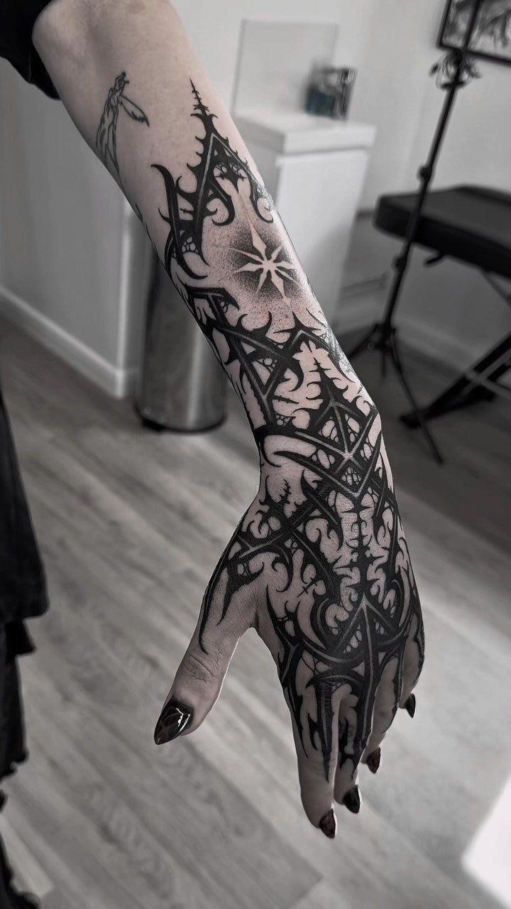 Intricate solid black geometric tattoo covering a person's hand and forearm