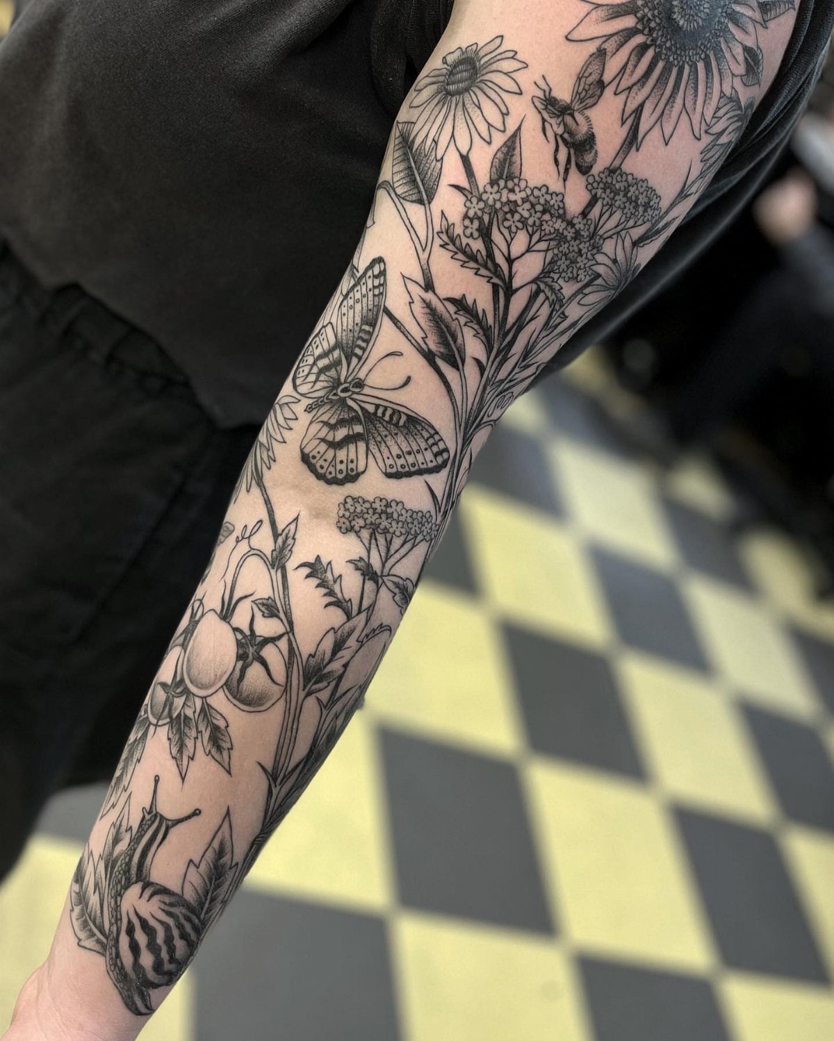 Black ink tattoo of vines, flowers, and a butterfly on a person's arm