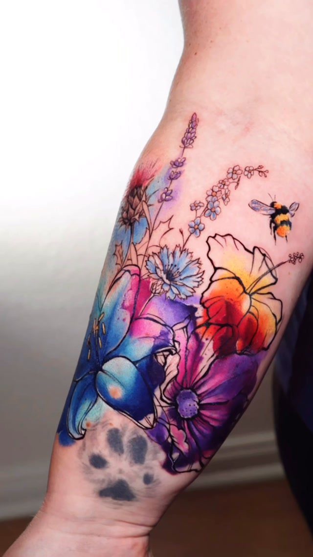 Colorful watercolor style tattoo of flowers and a bee on a forearm
