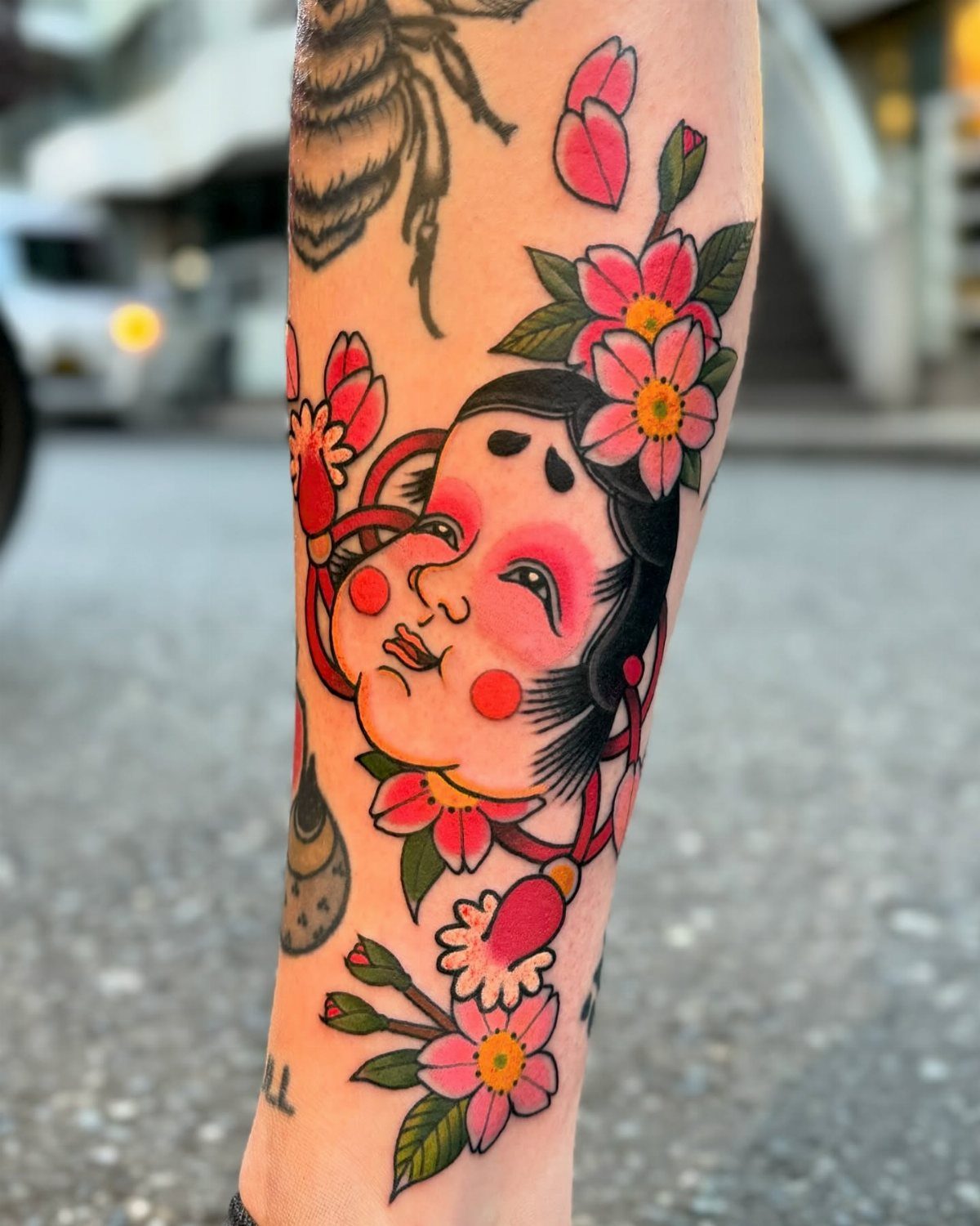 Japanese style tattoo of a face with pink cherry blossoms on an arm