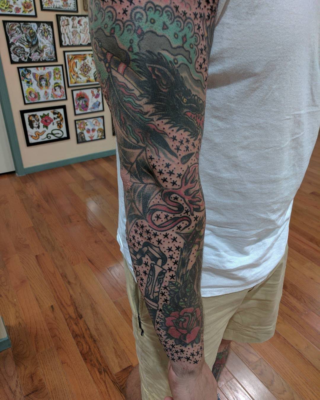 Tattooed arm sleeve with a dragon and rose filled with small black stars and dots.