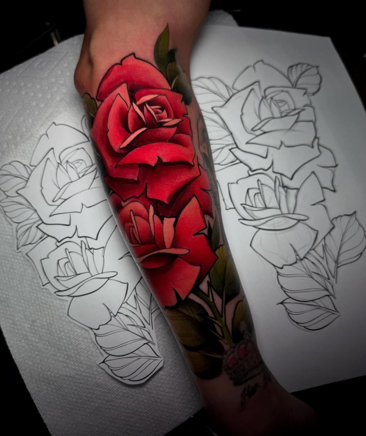 Red rose tattoo on a forearm next to its original line drawing.
