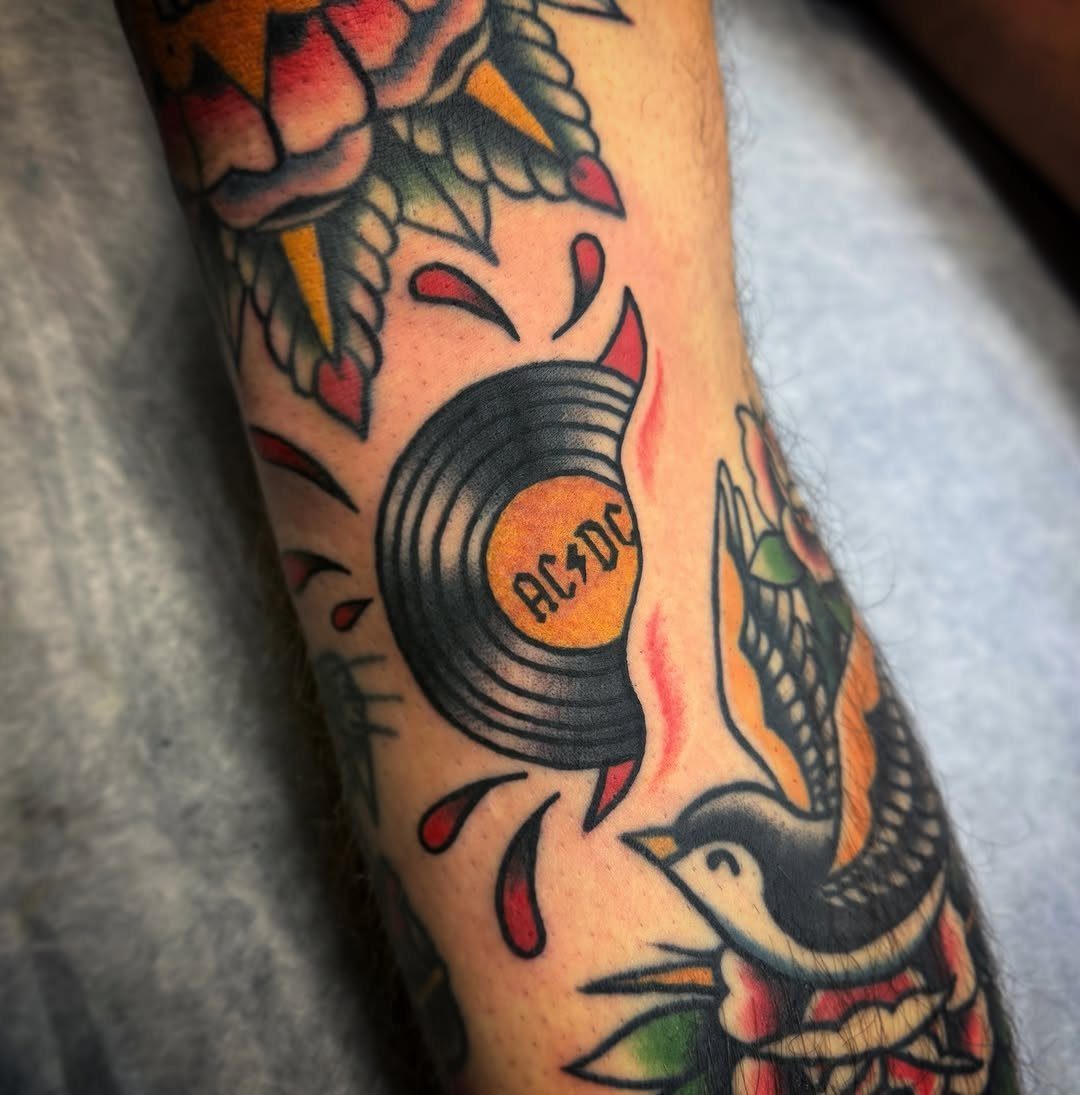 Vinyl record tattoo with AC/DC label on a person's tattooed arm.