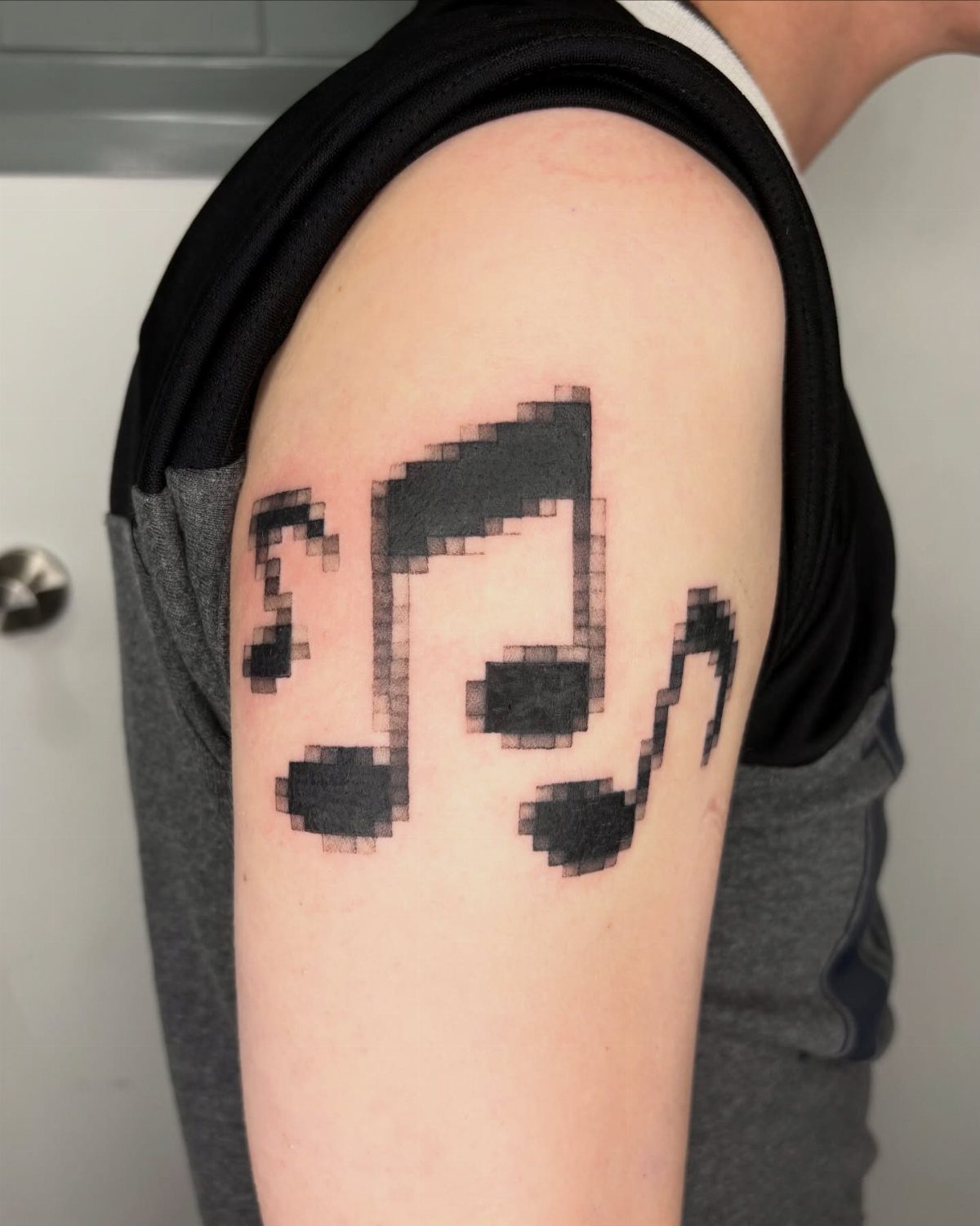 Pixelated music note tattoos on a person's upper arm in black ink.