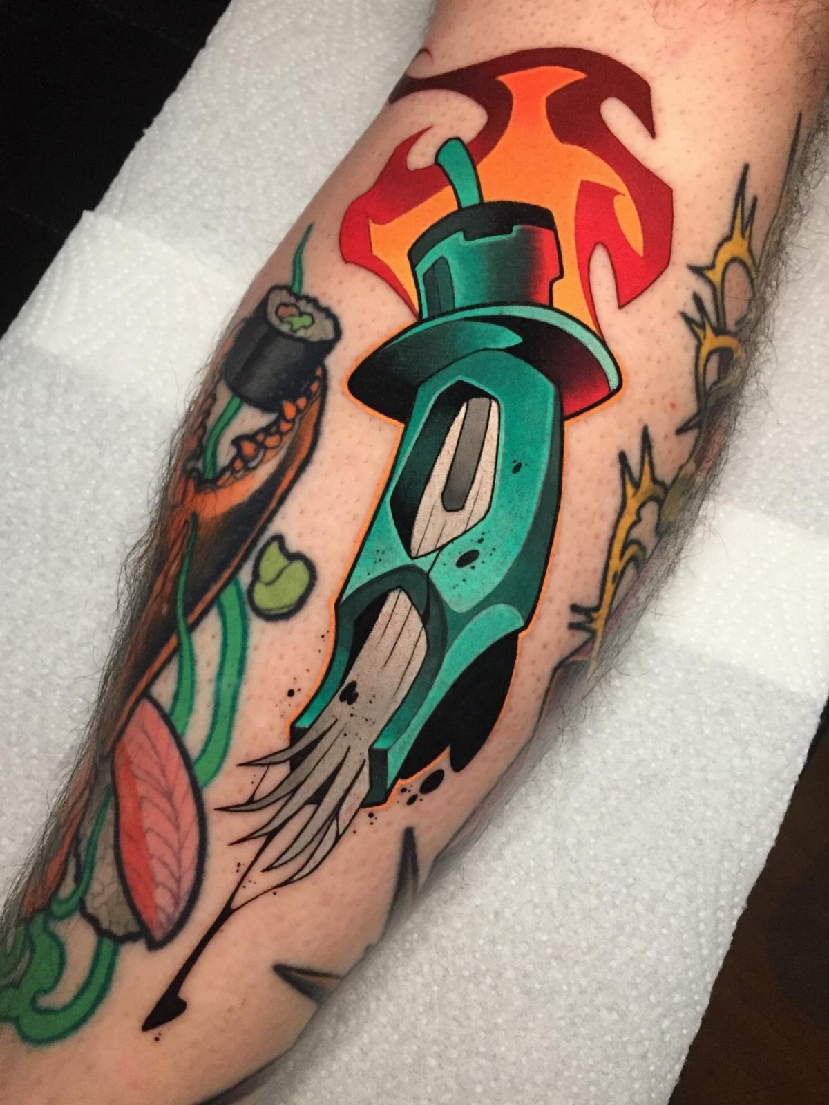 Teal rocket ship tattoo with orange flames on a person's arm.