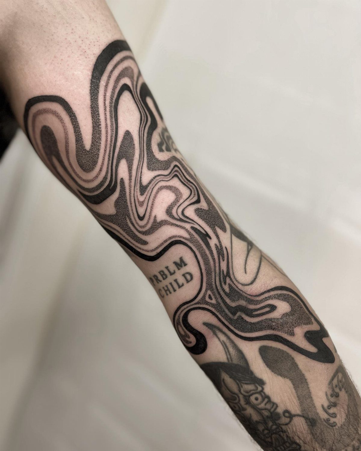 Wavy black ink tattoo with marbled swirls on a person's forearm