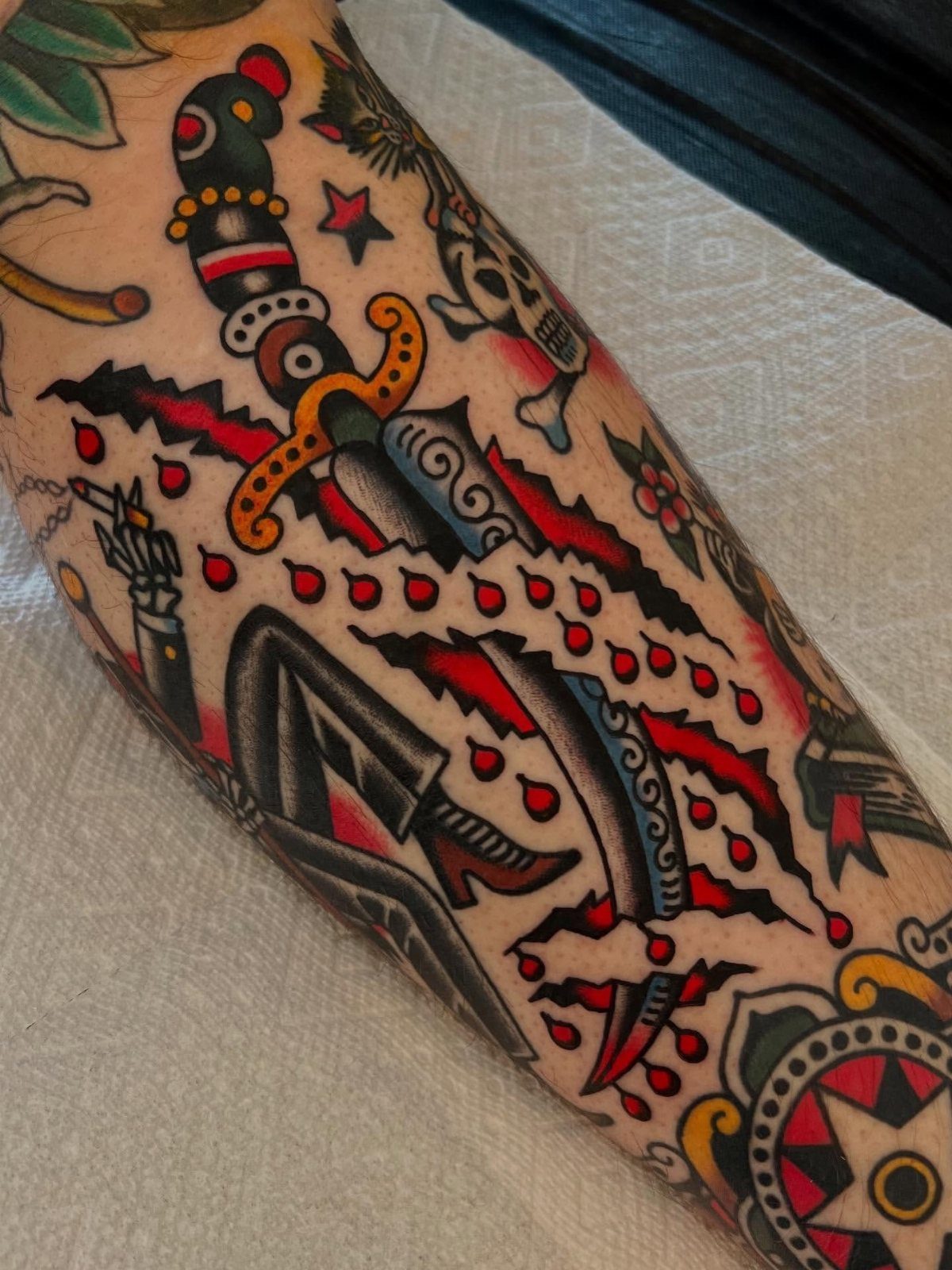 Traditional style tattoos on an arm featuring a dagger and various filler elements.