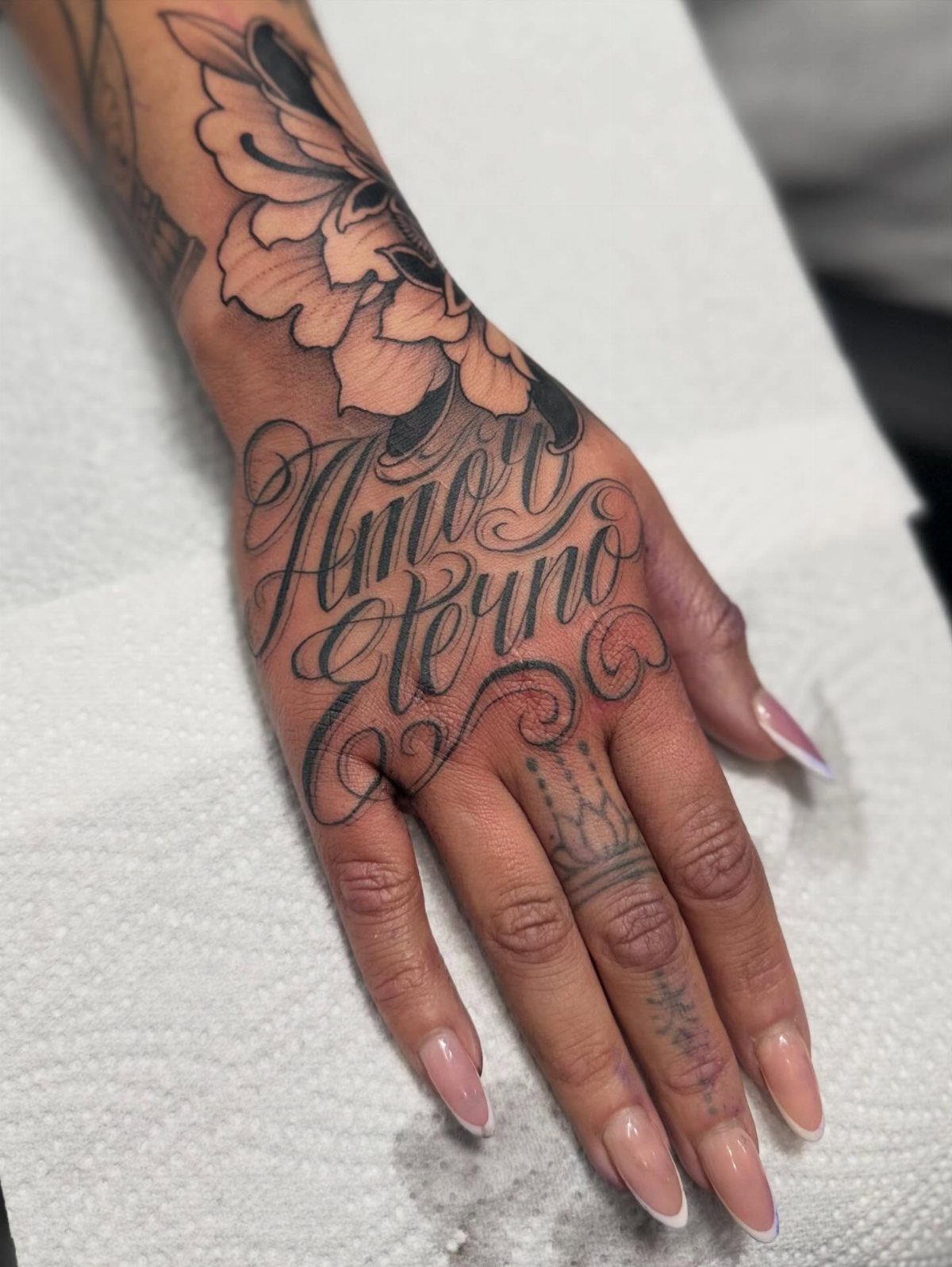 Tattooed hand with the cursive phrase Amor Eterno and a floral wrist piece