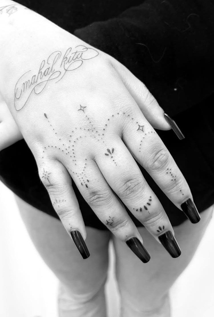 Hand with small dot and star tattoos and script on the back.